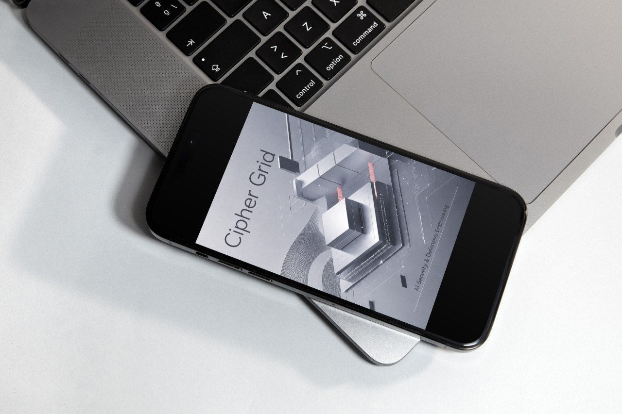 A black smartphone lying diagonally on top of a silver laptop, with the phone screen displaying the text 'Cipher Grid'.