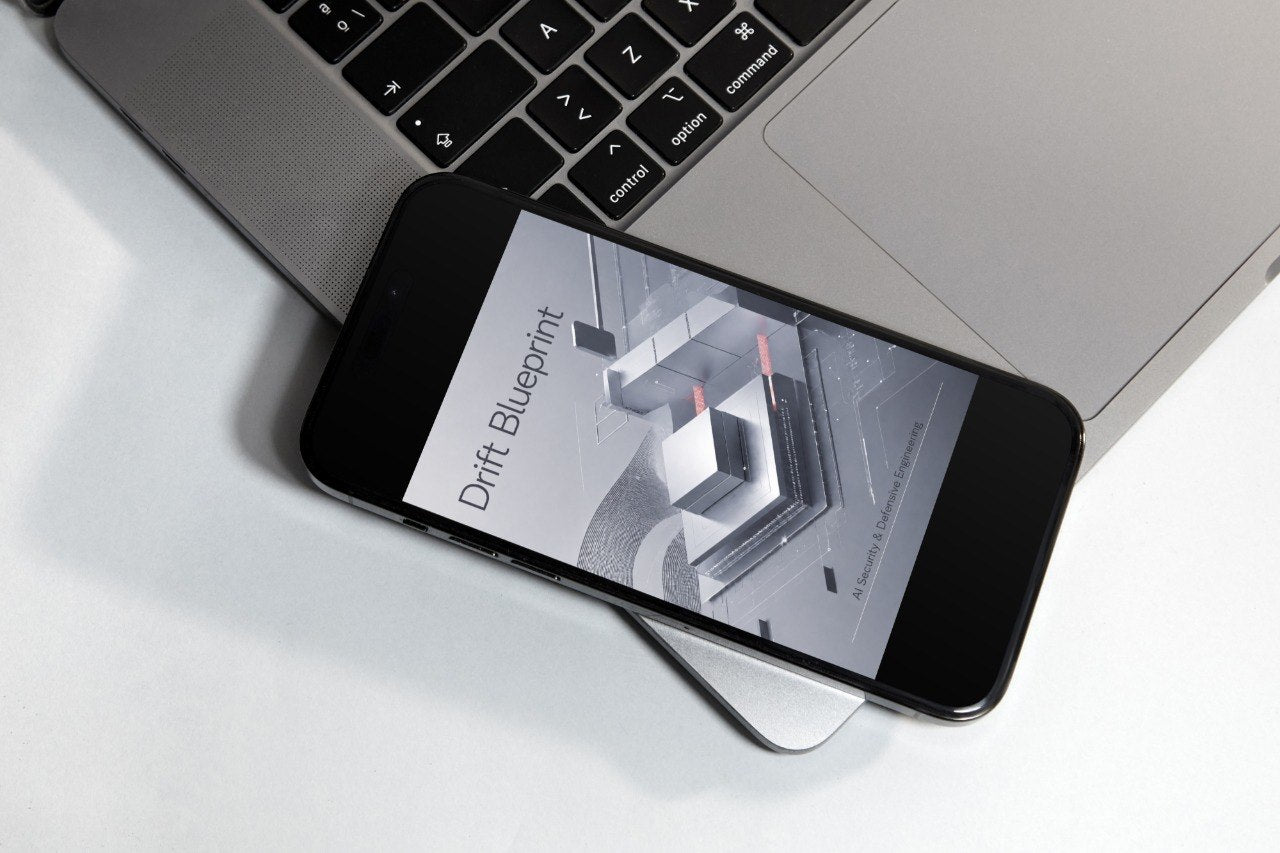 A black smartphone lying diagonally on top of a silver laptop on a white surface, with the phone screen displaying the text 'Drift Blueprint'.